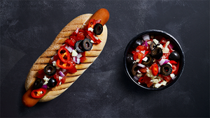 En pølse med tomatsalsa og en liten skål med salat ved siden av på en svart bakgrunn.