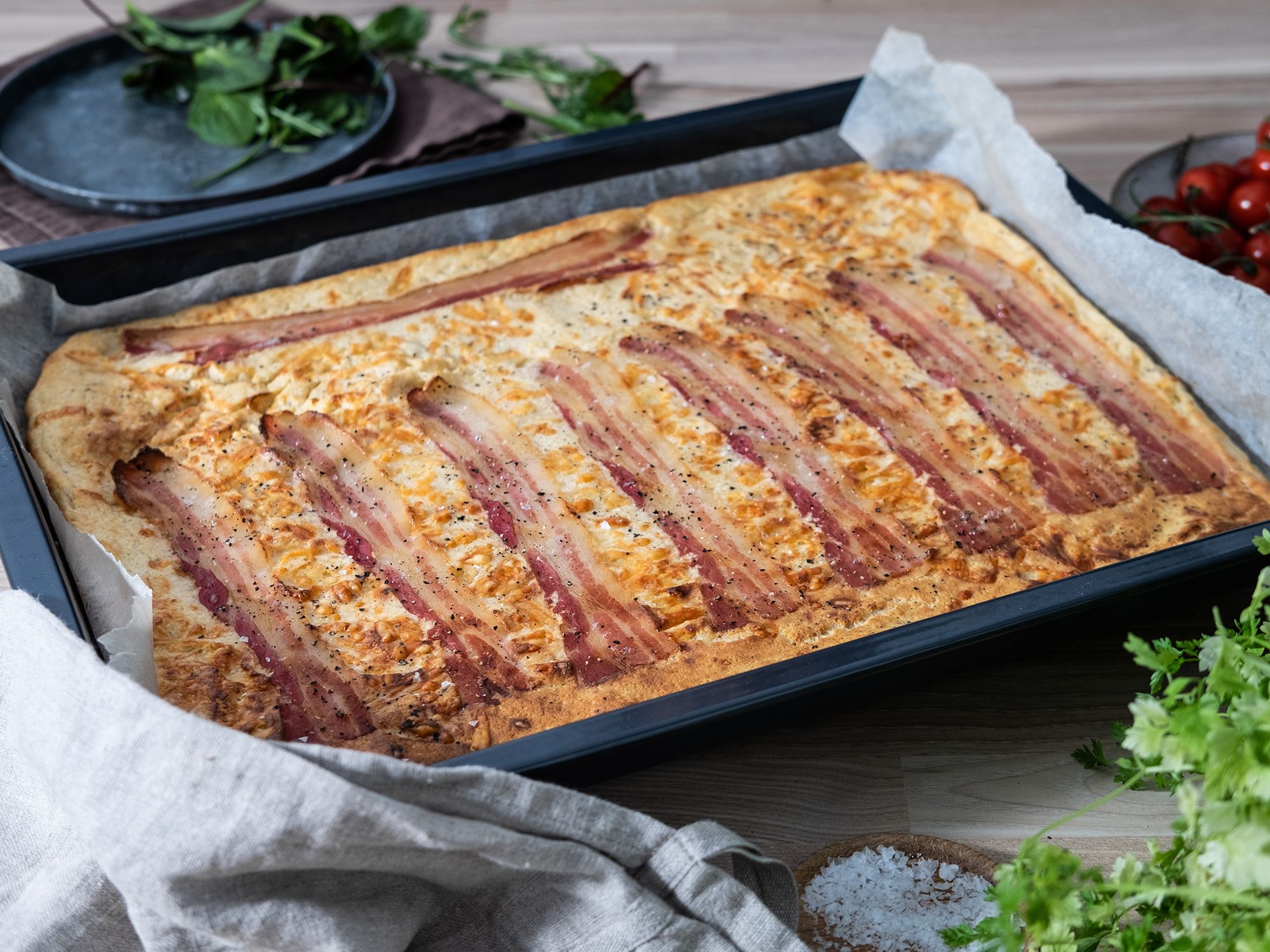 Pannekake med bacon og ost i ovn på en bakeplate med bakepapir.