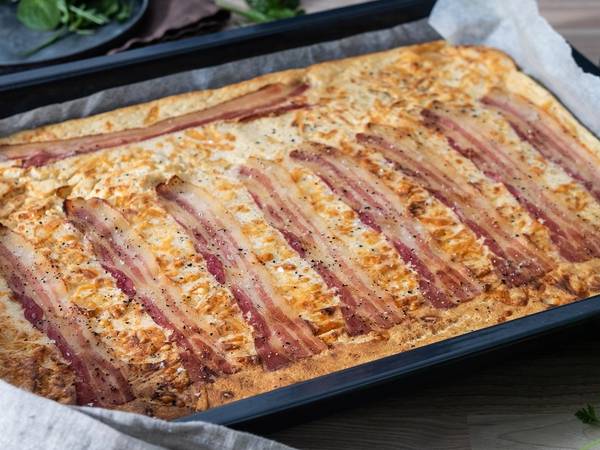 Pannekake med bacon og ost i ovn på en bakeplate med bakepapir.