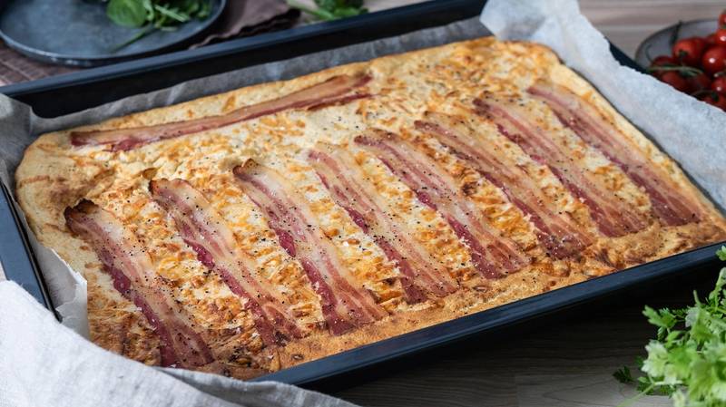 Pannekake med bacon og ost i ovn på en bakeplate med bakepapir.