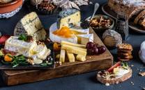 Et utvalg av oster, kjeks og frukt på et serveringsbord, med ulike typer ost og tilbehør.