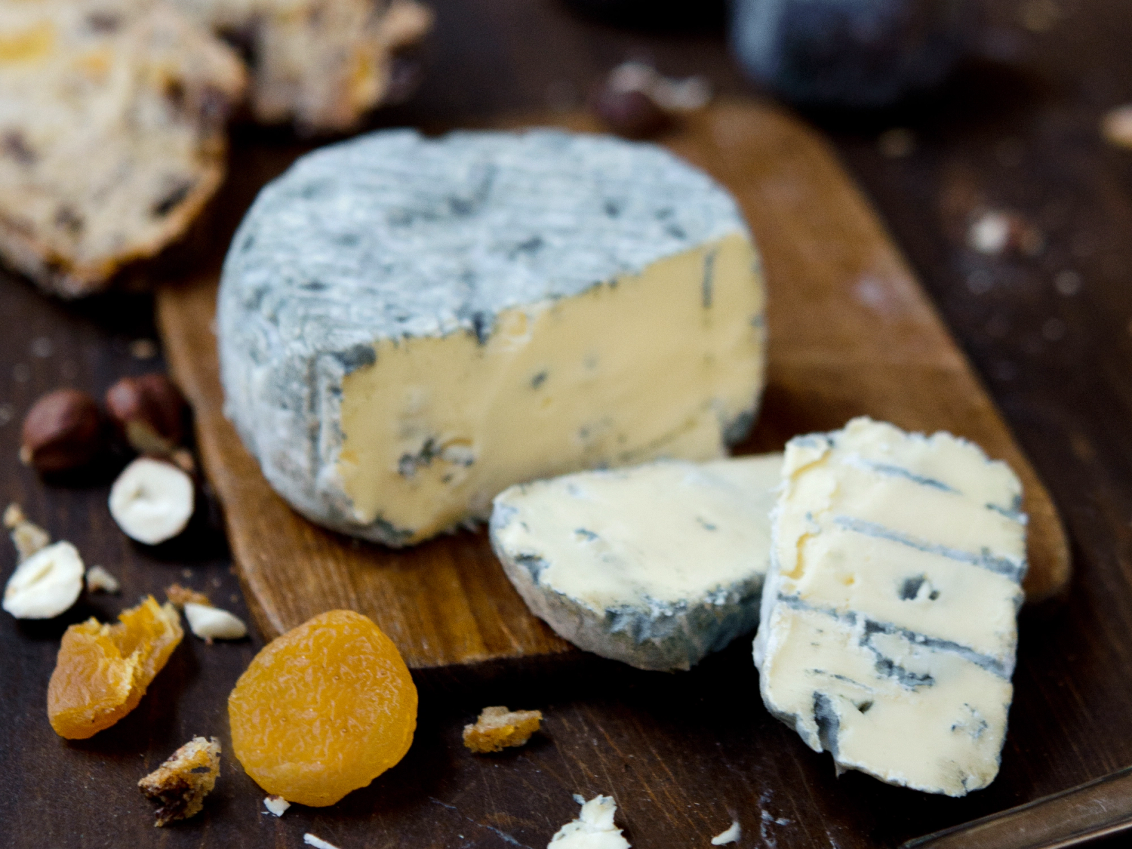 Ulike typer blåmuggost på et trebord med noen kjeks og tørket frukt rundt.