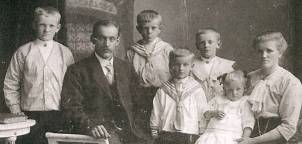 En gruppe barn og en voksen står sammen utendørs, med en bygning i bakgrunnen, på et gammelt svart-hvitt bilde.