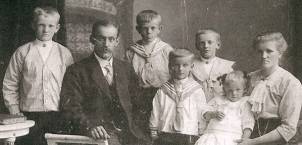 En gruppe barn og en voksen står sammen utendørs, med en bygning i bakgrunnen, på et gammelt svart-hvitt bilde.