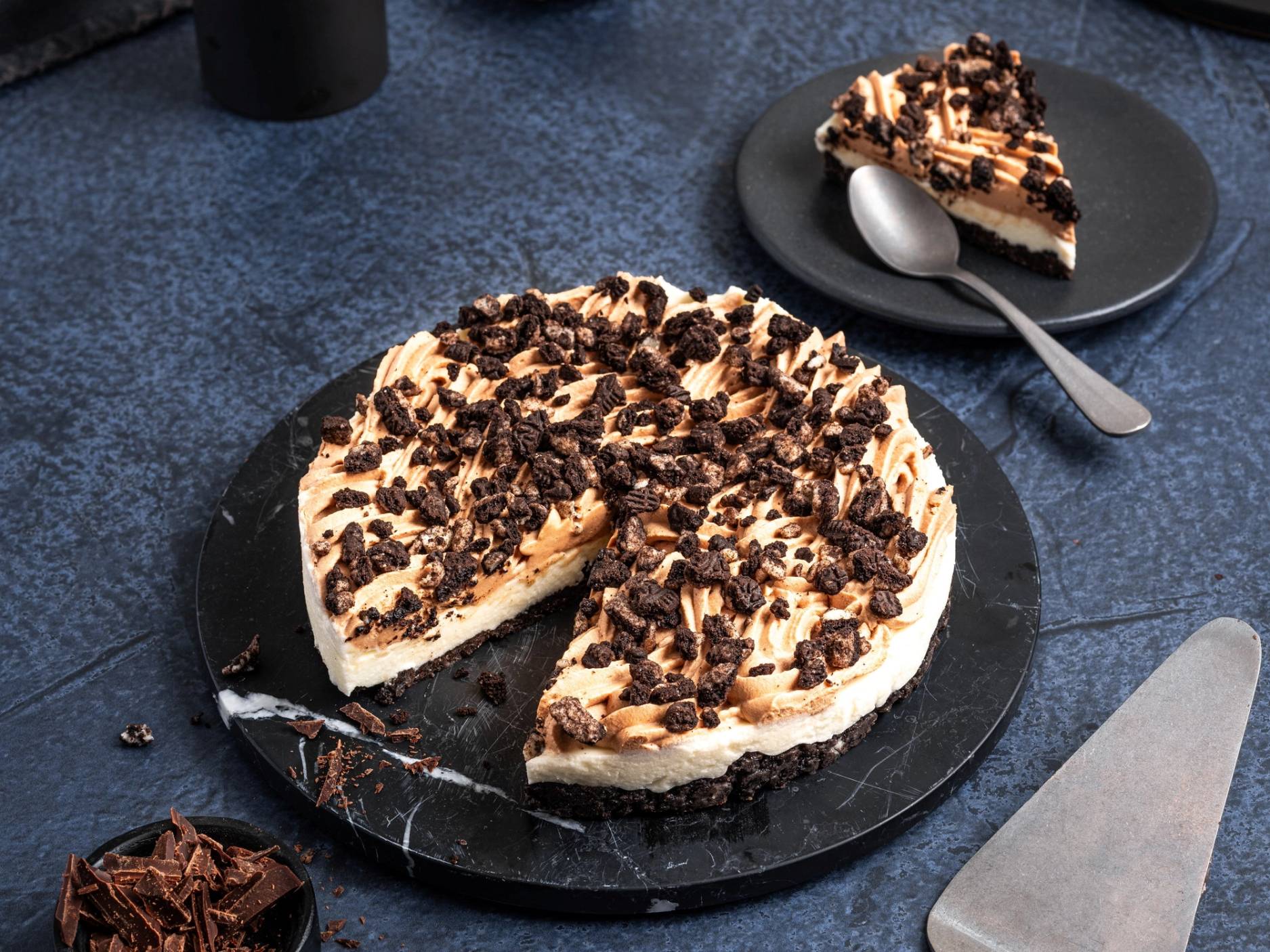 En kake med sjokoladekrøller på toppen, delvis skåret opp, plassert på en svart tallerken på en mørk blå bakgrunn.