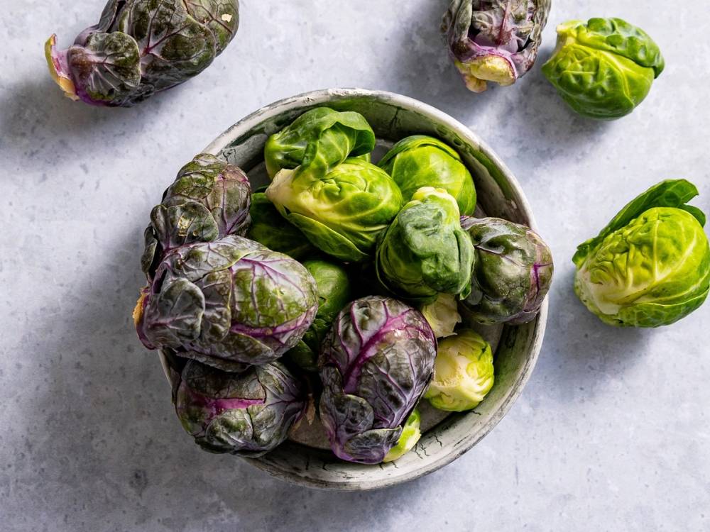 En skål med ulike typer rosenkål, noen grønne og noen lilla, på en lys overflate.