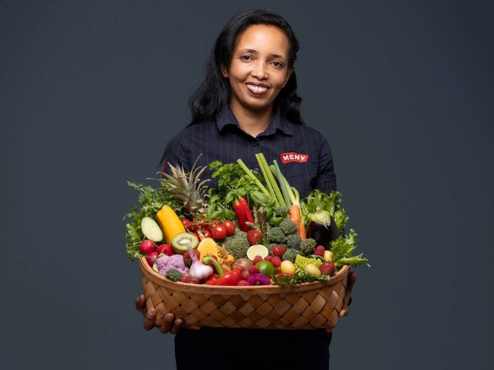 Person holder en kurv full av frukt og grønnsaker.