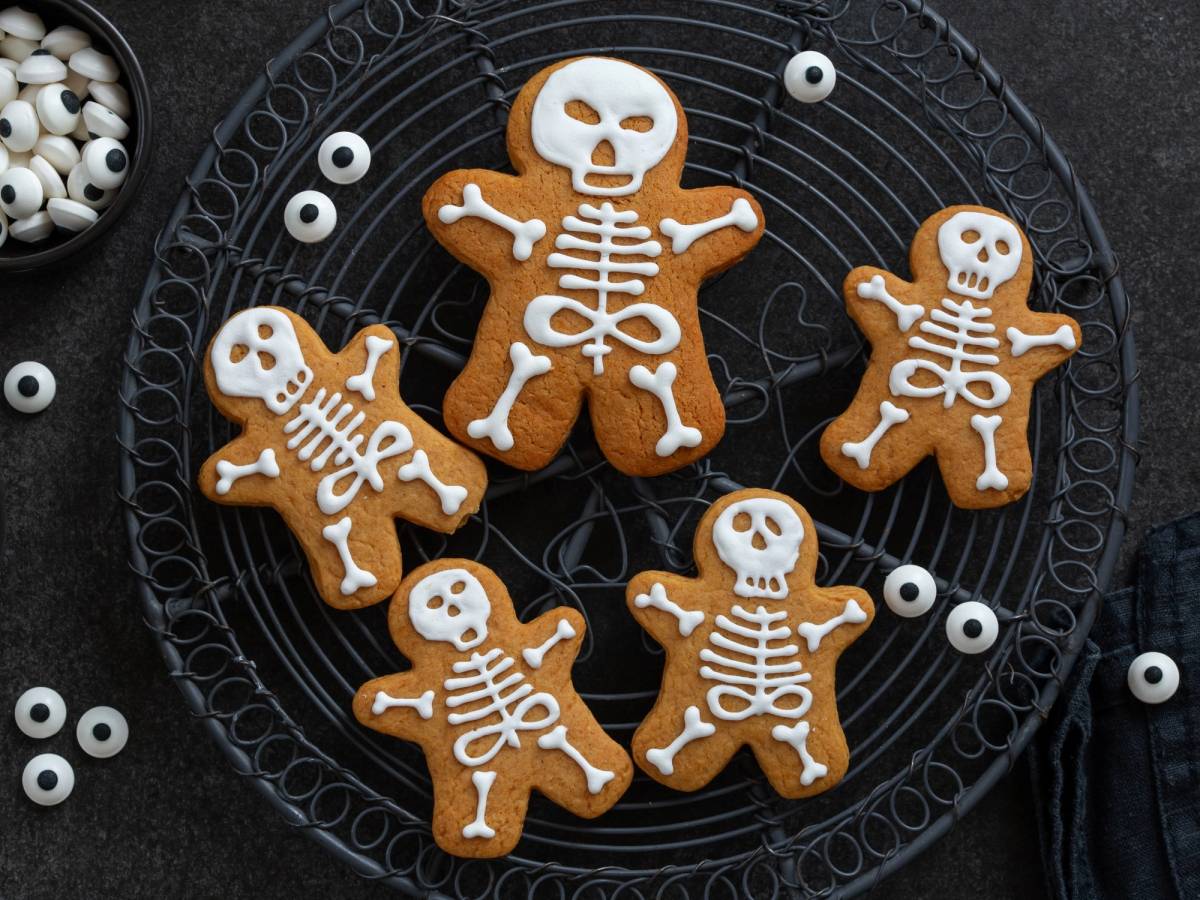 Halloween-kjeks formet som skjeletter og en skjeletthodeskalle på en svart rist med hvite kuler rundt.