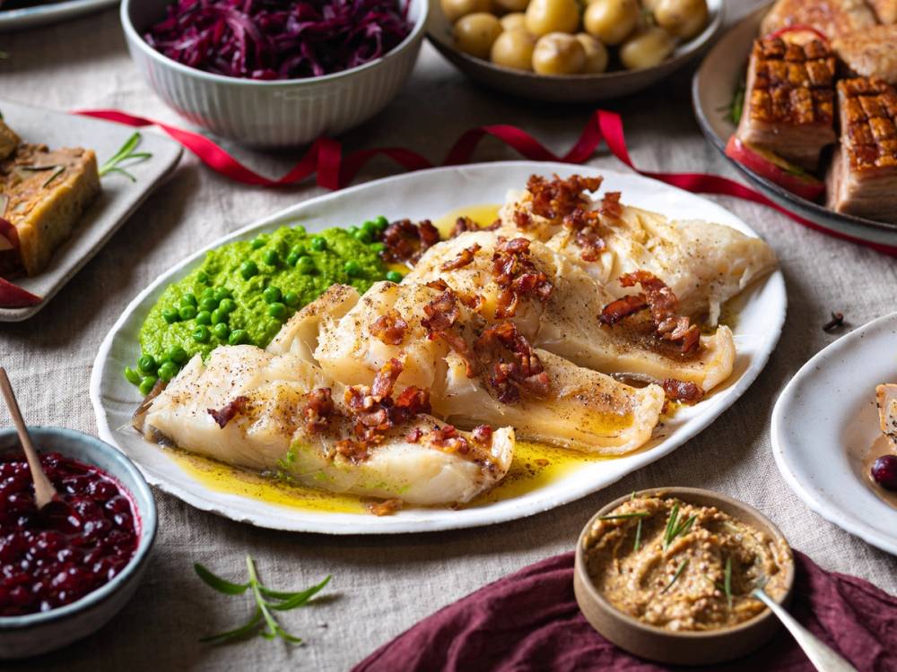 Julebord med stekt fisk, grønnsaker og tilbehør på et dekket bord.