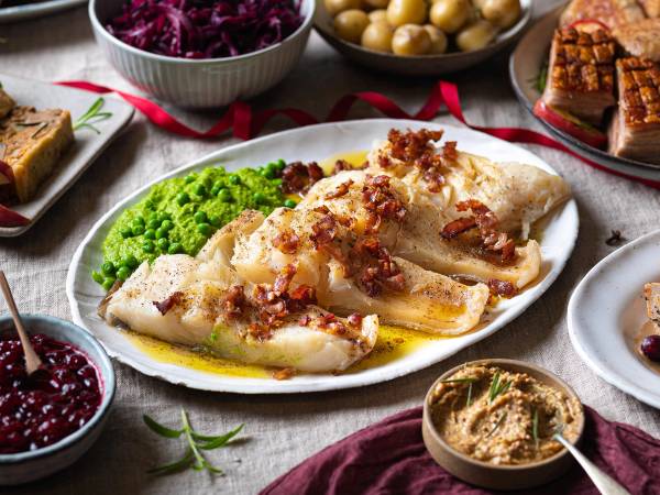 Julebord med stekt fisk, grønnsaker og tilbehør på et dekket bord.