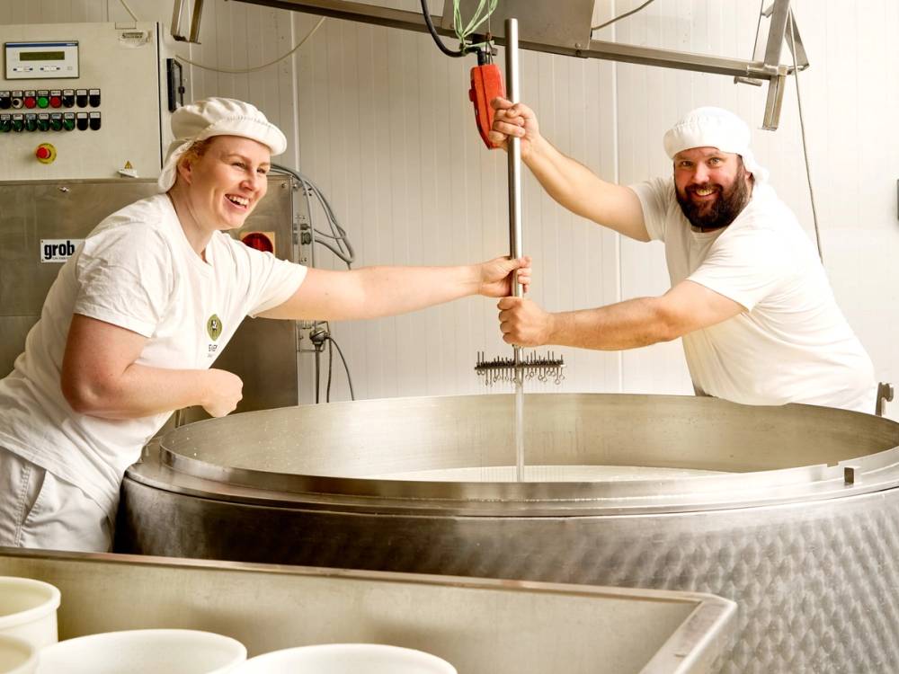 To personer i hvite klær jobber med en stor industribasseng i et produksjonsmiljø, og holder i en løfteanordning over bassenget.