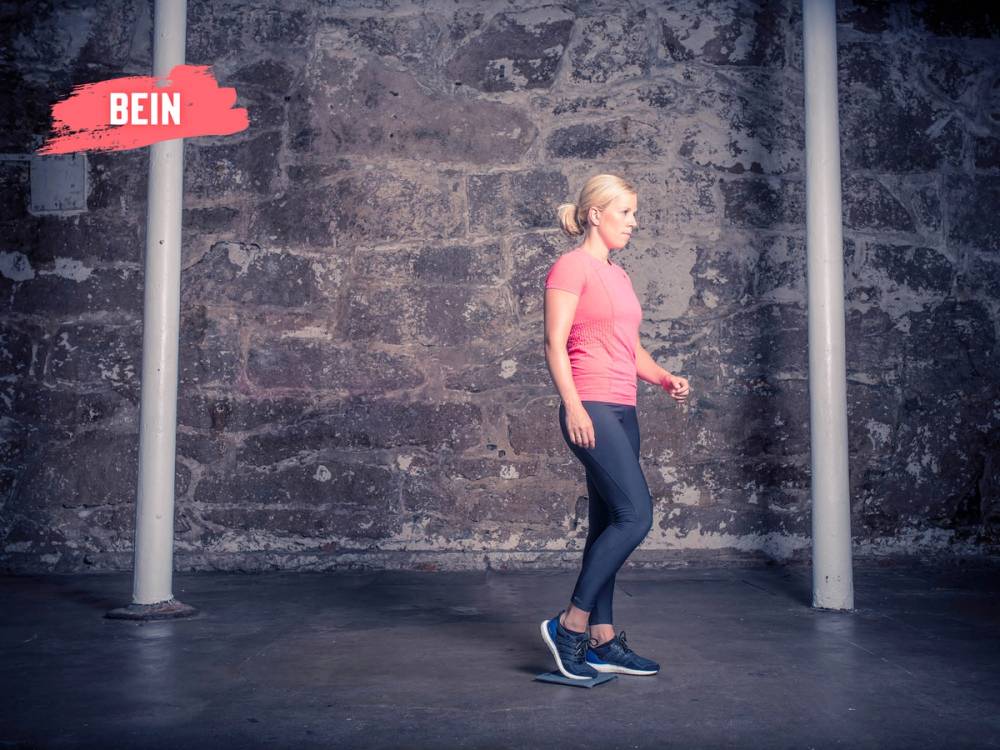 En person står ved en sklimatte i et treningsrom, klar til å hoppe eller klatre opp, med en murvegg i bakgrunnen.