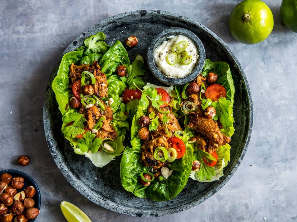 Vegetariske tacos servert i hjertesalat med grønnsaker og nøtter på en svart tallerken