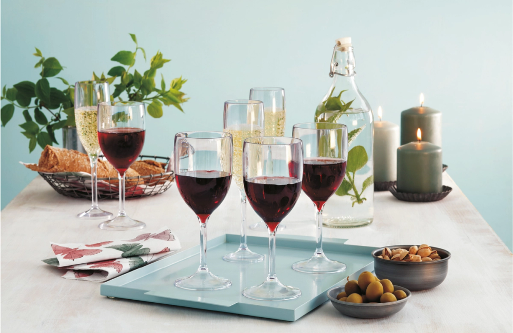 Et bord med fire glass med rødvin, en flaske vann, nøtter og en plante i bakgrunnen, dekorert med stearinlys.