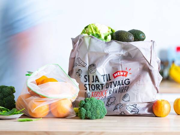En gjenbrukspose fylt med grønnsaker og frukt på kjøkkenbenken, med en blå klesplagg i bakgrunnen.