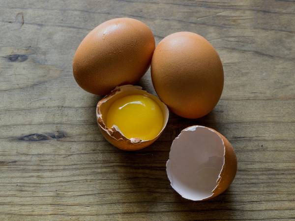 To hele egg og et halvt egg med flytende eggeplomme på en treplate