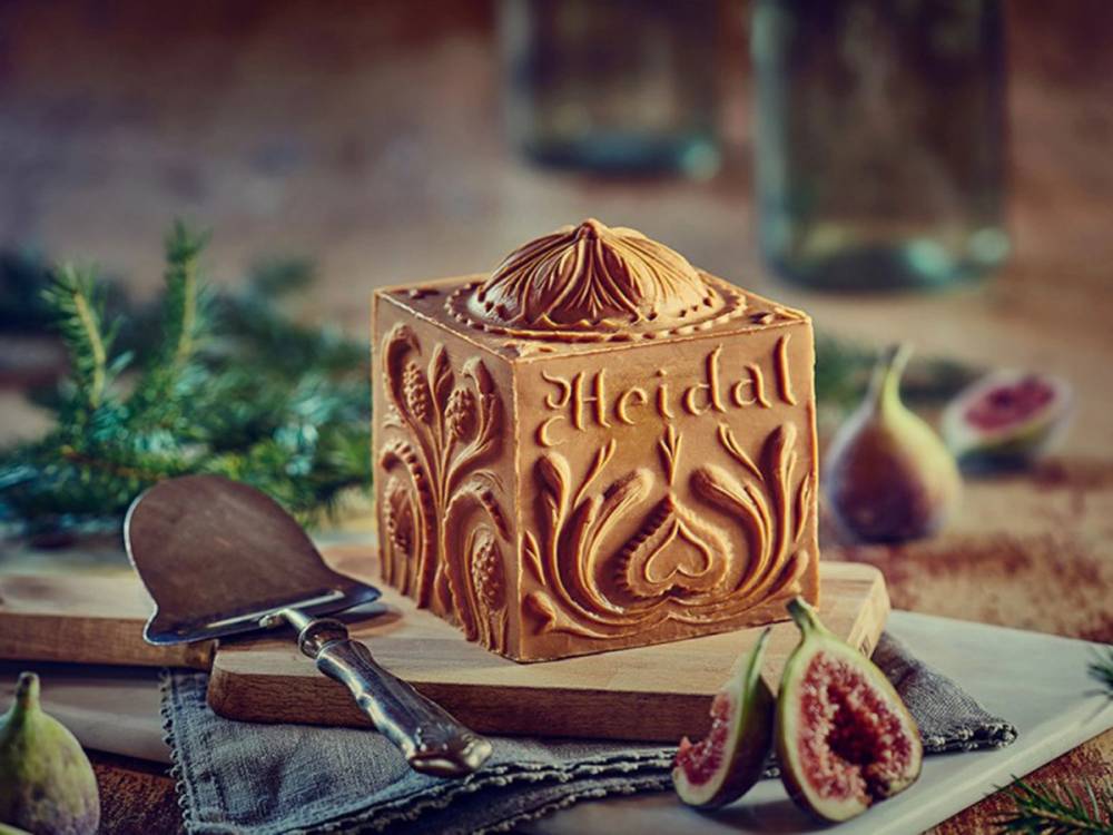 En kake med heidal-motiv og navnet 'Heidal' på, plassert på et bord med frukt og blader rundt.