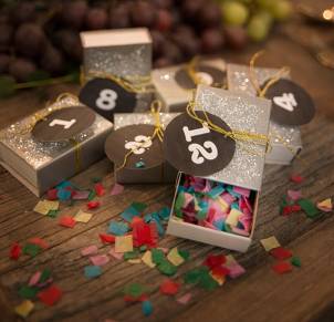 Små gaveesker med tall på, fylt med konfetti og pynt, brukt som festtilbehør.