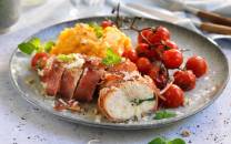 Kyllingbryst fylt med manchago ost og surret i spekeskinke, servert med potetmos og cherrytomater på en tallerken.