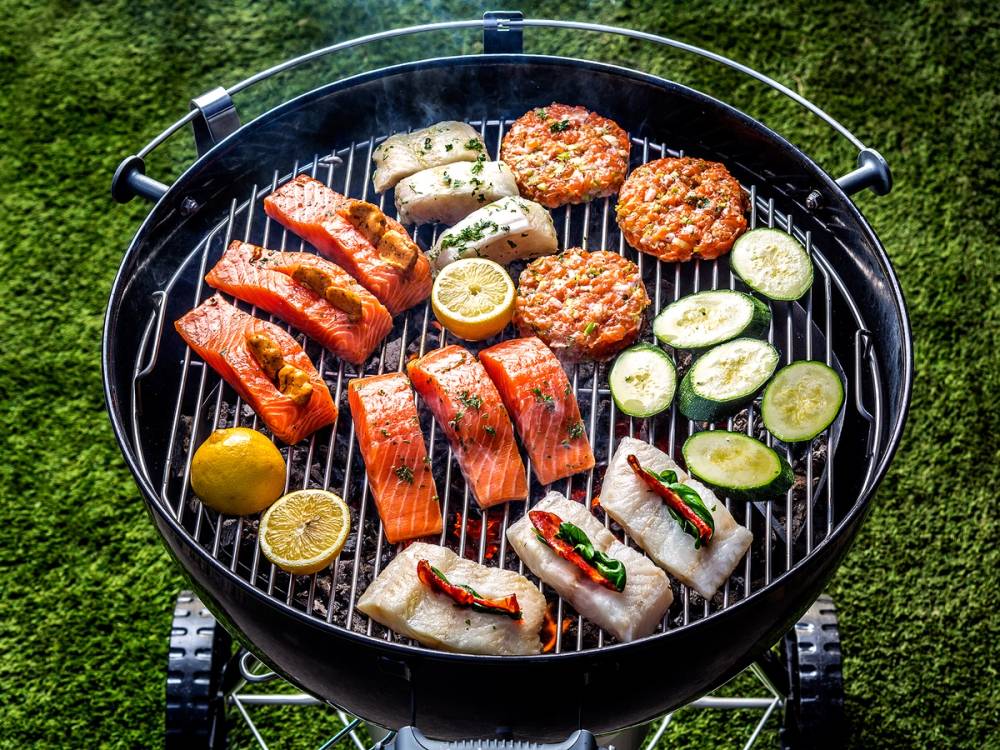 Grill med ulike typer kjøtt, grønnsaker og sitroner på en uteplass med gressbakgrunn