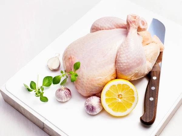 Hel kylling plassert på en skjærefjøl med sitron, hvitløk og urter, klar for tilberedning.