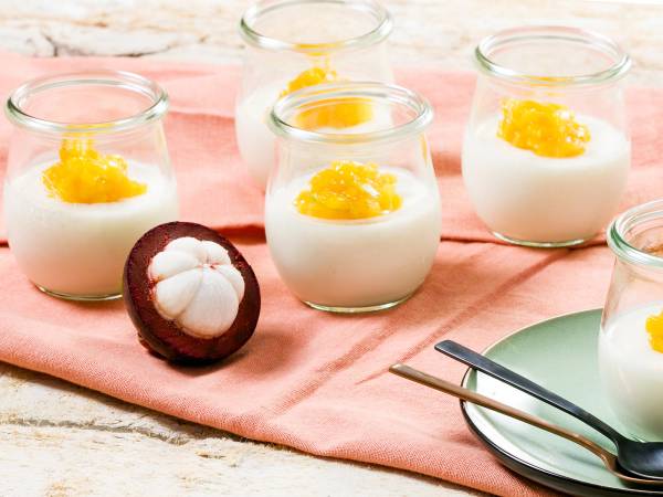 Mangostanfrukt og små glass med yoghurt og mangostanbiter på et bord.
