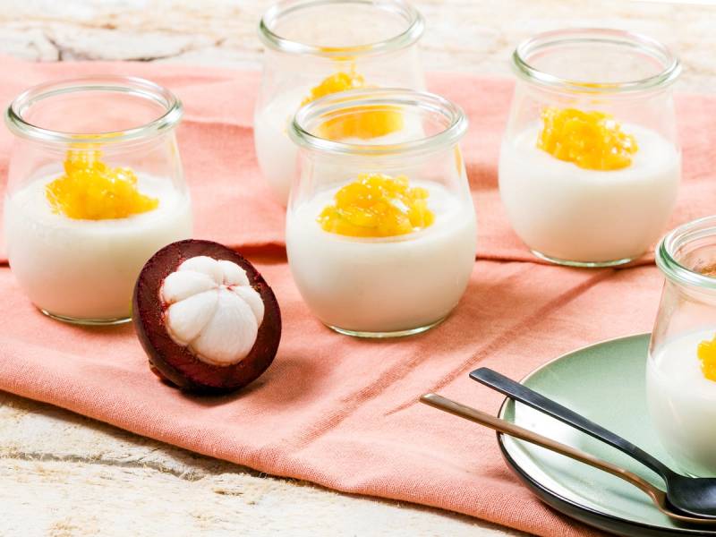 Mangostanfrukt og små glass med yoghurt og mangostanbiter på et bord.