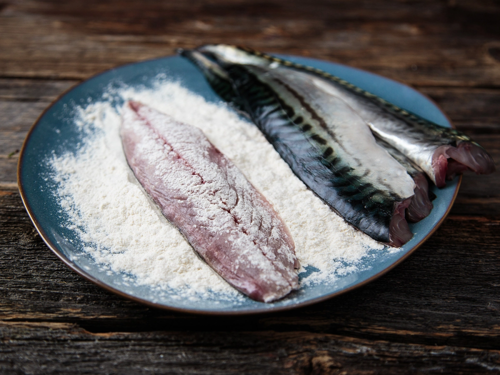 To makrellfileter ligger på en blå tallerken med mel, klar til tilberedning.