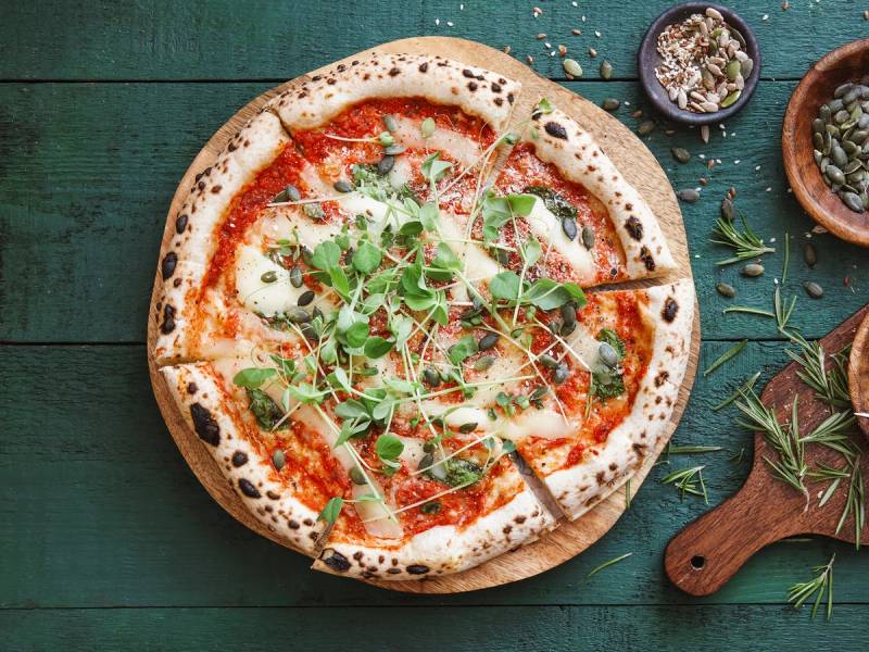 Vegan pizza margherita med tomatsaus, ost og friske urter på en grønn treplate.