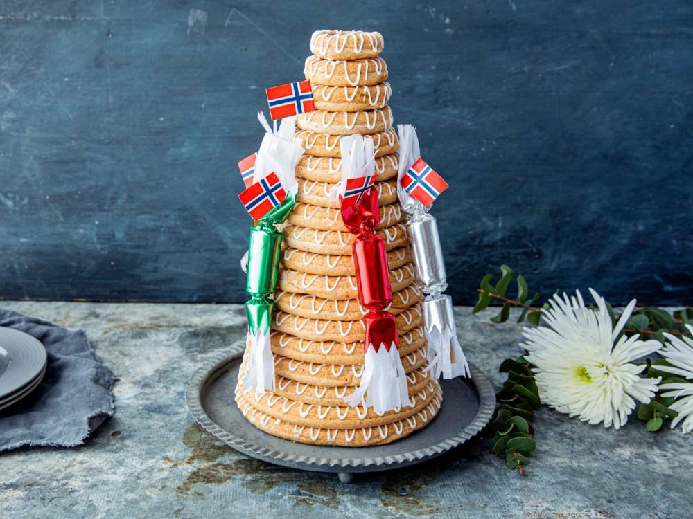 En kransekake pyntet med norske flagg og dekorasjoner på et fat, klar til å bli servert til feiring.