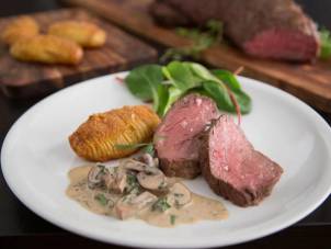 Helstekt indrefilet med hasselbackpoteter, kremet sopp og en liten salat på en hvit tallerken.