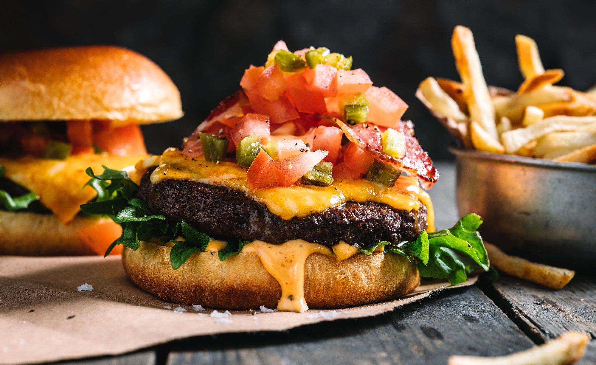 En spicy burger med kjøttdeig, ost, salat, tomat og salsa, servert med pommes frites på siden.