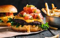 En spicy burger med kjøttdeig, ost, salat, tomat og salsa, servert med pommes frites på siden.