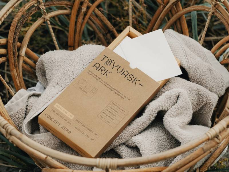 En pappeske med to-wash arkmateriell ligger i en kurv omgitt av et håndkle og tørkede planter i bakgrunnen.