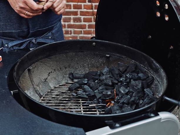 Grillkull med indirekte varme i en kullgrill, klar til grilling, med en person i bakgrunnen.
