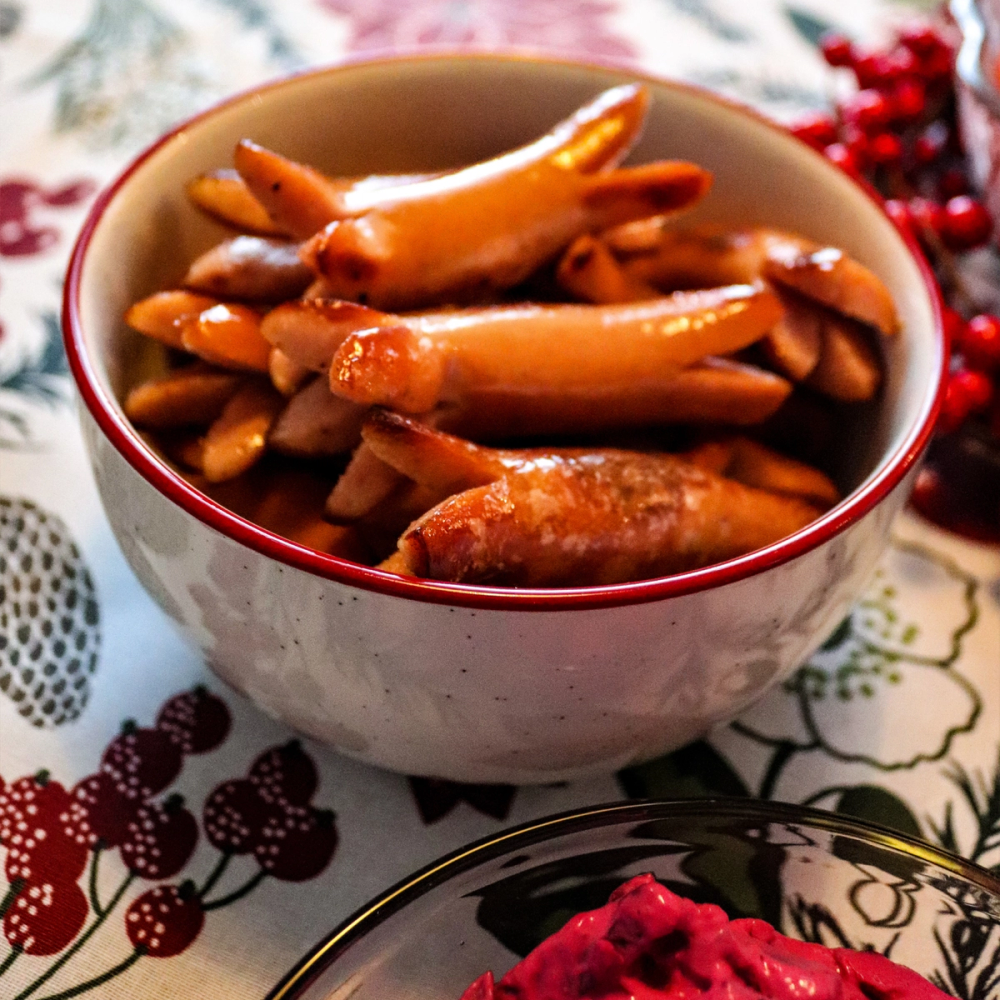 Svensk prinskorv til jul i en hvit bolle med rød kant, plassert på et juledekket bord.