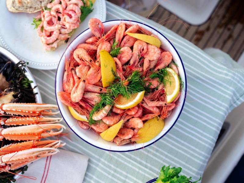 En bolle med reker, sitronskiver og grønn dill på et bord dekket med en blå og hvit striped duk.