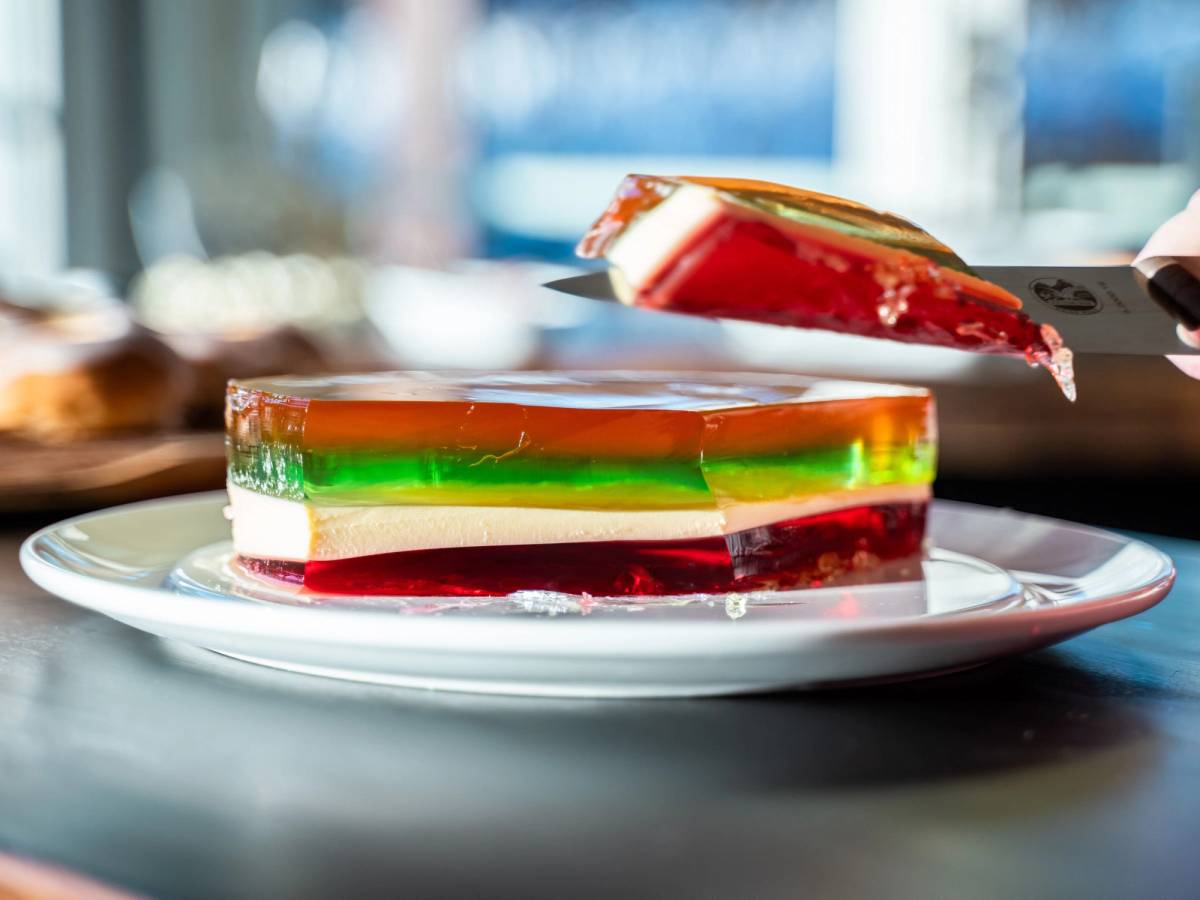 Et lagdelt ostekake med grønne, gule og røde lag på en hvit tallerken, med en skje som har tatt en bit av kaken.