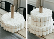 En kake laget av flere hvite marshmallows stablet i lag, med en tom papprull på toppen, plassert på et bord i et kjøkken.