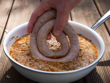 En person holder en pølse over en bolle med ølbad, klar til å bli kokt eller grillet.