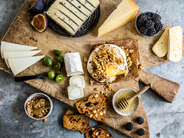 Et ostefat med ulike typer ost, kjeks, druer og honning på en treplate, med en skje og en liten bolle med honning ved siden av.