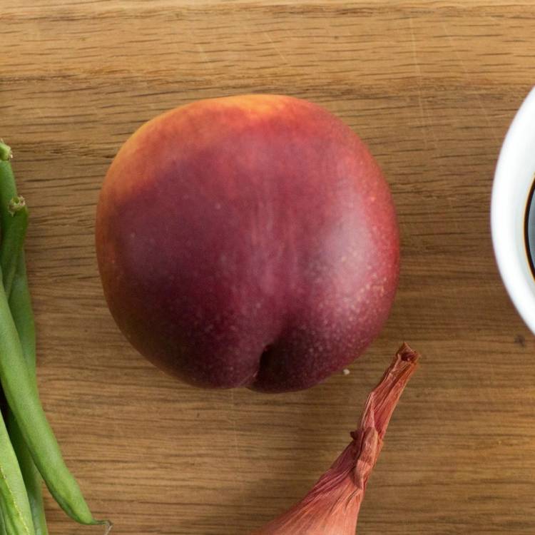 En fersken på et trebord med en del av en hvit kopp synlig til høyre.