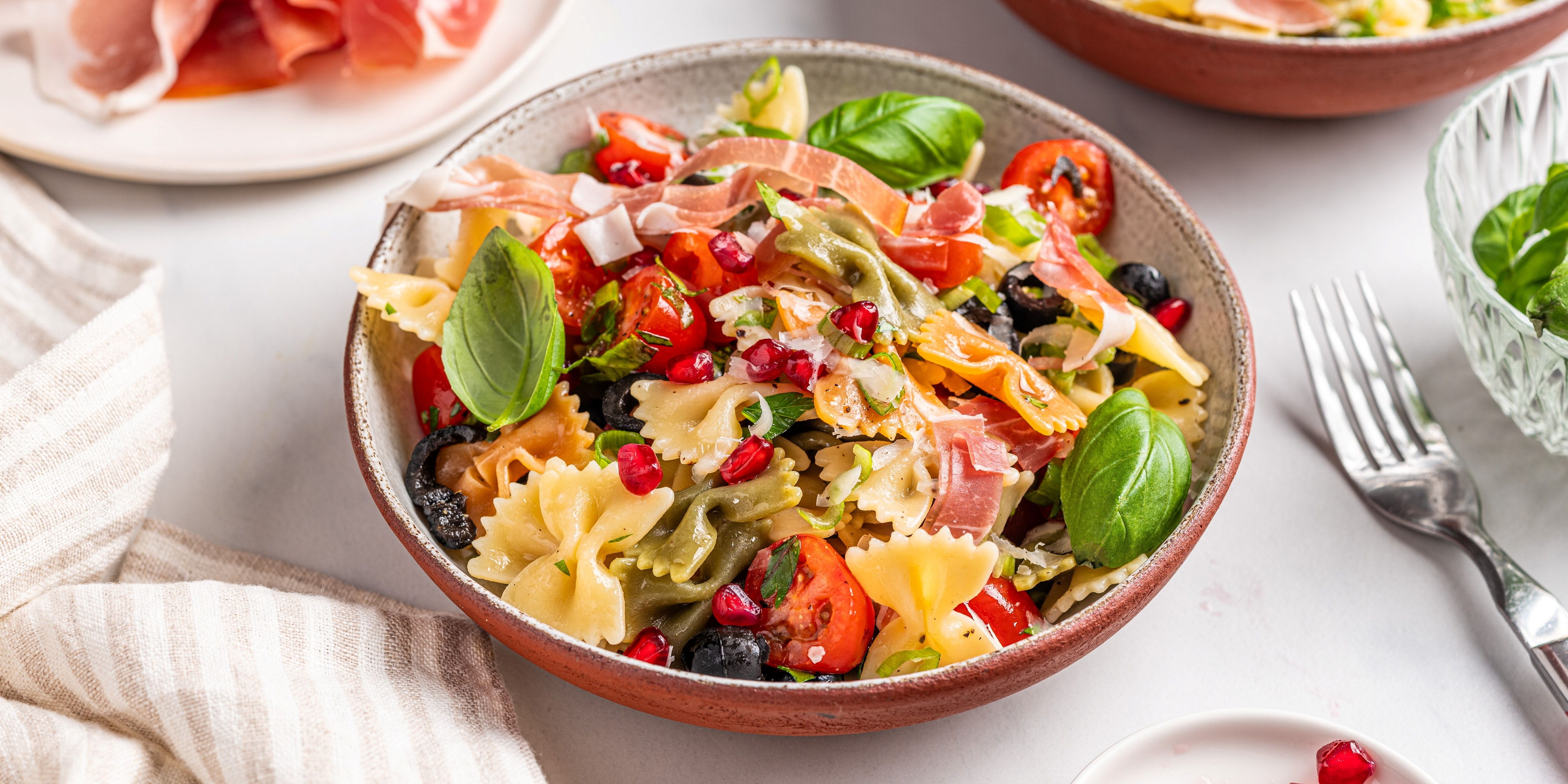 Farfalle pasta med middelhavsgrønnsaker og friske basilikumblader i en bolle.