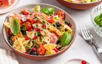 Farfalle pasta med middelhavsgrønnsaker og friske basilikumblader i en bolle.