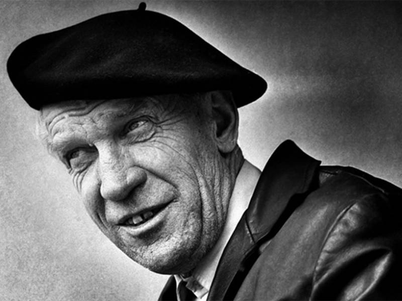 En person med mørk hatt og jakke, sett fra siden, på et svart-hvitt bilde.