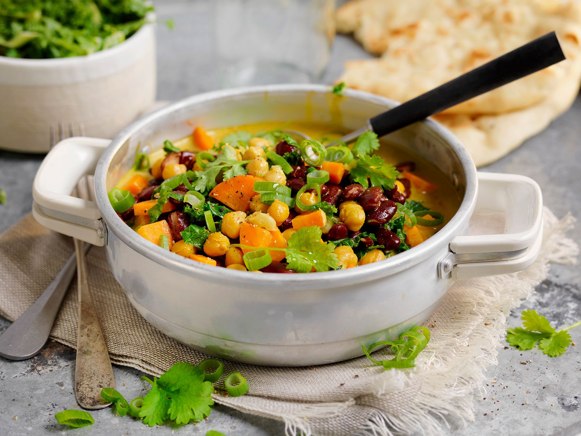 En vegetarisk gryte med kokosmelk, gulrøtter, kikerter og grønnsaker i en hvit gryte på et bord.