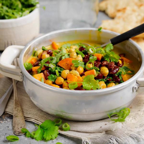 En vegetarisk gryte med kokosmelk, gulrøtter, kikerter og grønnsaker i en hvit gryte på et bord.