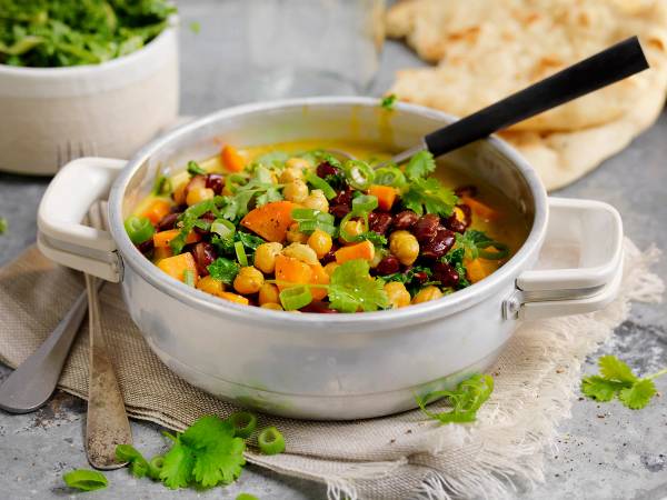 En vegetarisk gryte med kokosmelk, gulrøtter, kikerter og grønnsaker i en hvit gryte på et bord.