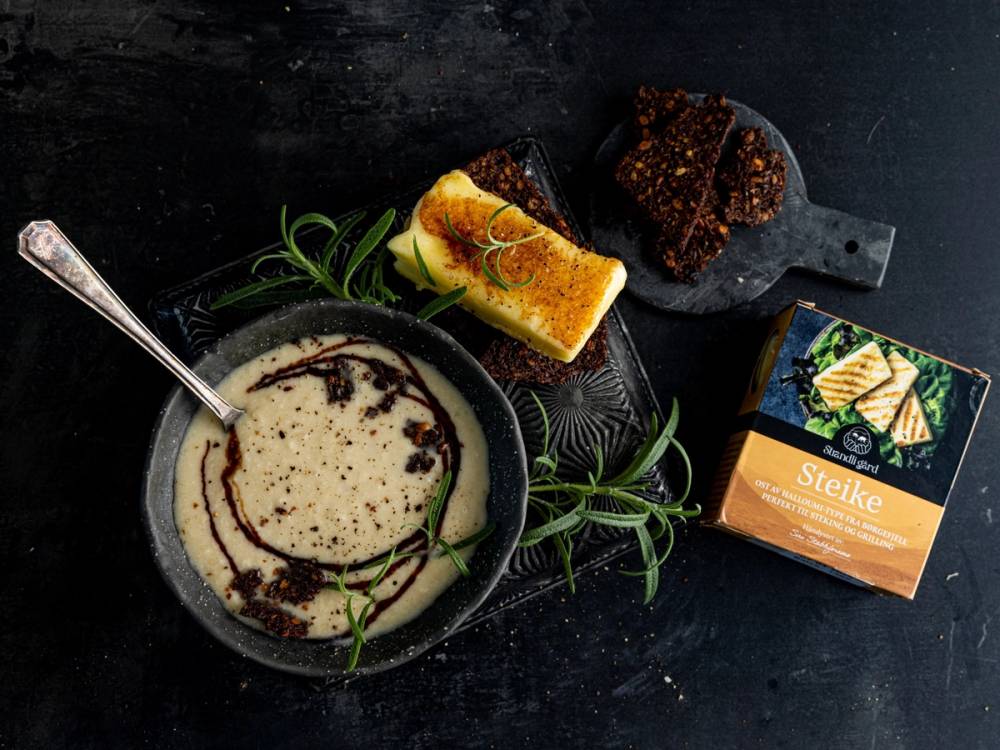 En skål med suppe, et stykke kake, en liten pakke med kjeks og noen urter på en svart bakgrunn.