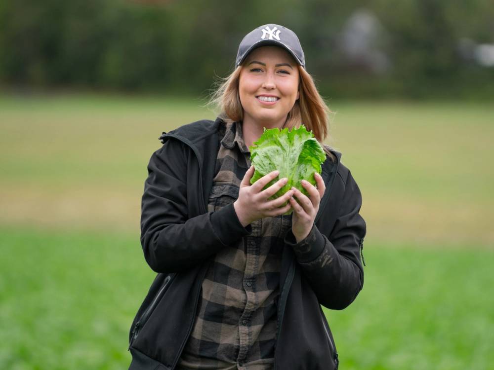 En person holder en stor grønn salat i hendene ute i en park, med trær og gress i bakgrunnen.